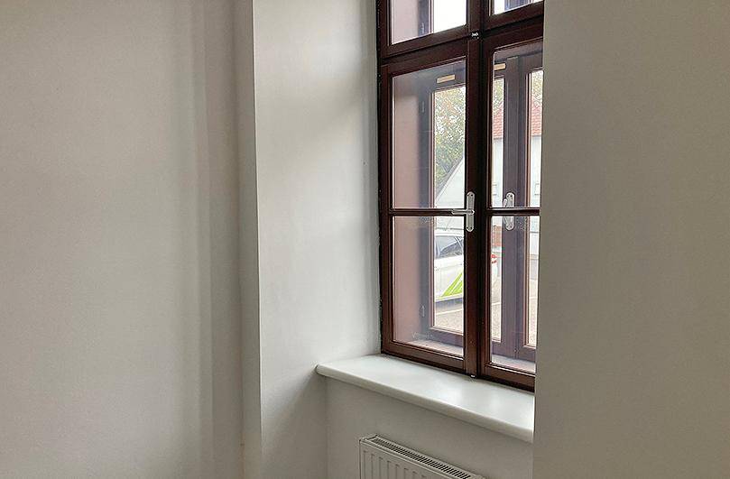 Heller Raum mit einem großen Fenster, weißer Fensterbank und Heizkörper unter dem Fenster.