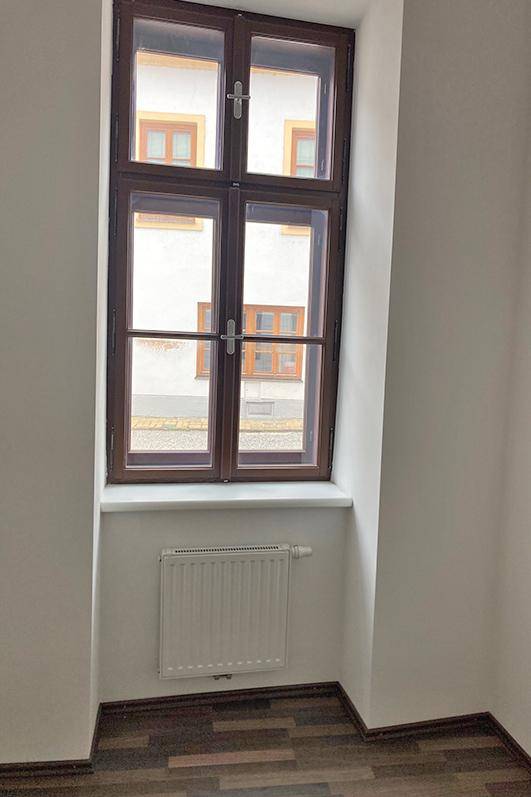 Heller Raum mit einem großen Fenster, dunklem Laminatboden und Heizkörper.