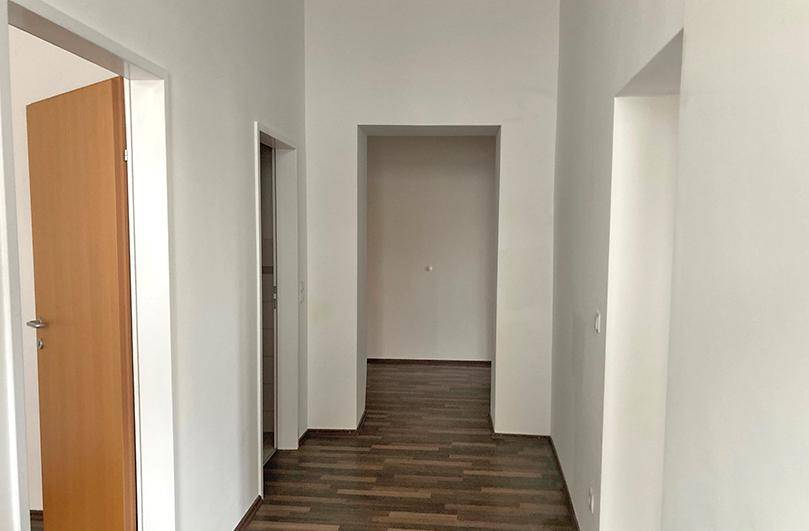 Heller Flur mit dunklem Laminatboden, weißen Wänden und mehreren Türöffnungen.