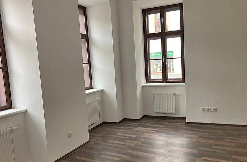 Heller Raum mit dunklem Laminatboden, weißen Wänden und mehreren Fenstern.