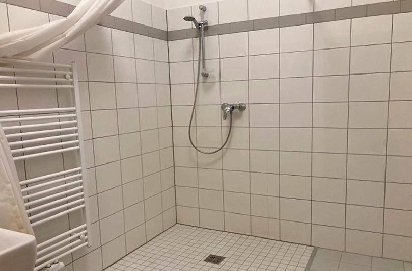 Gefliestes Badezimmer mit Duschbereich, Handtuchheizkörper und weißer Duschvorhang.