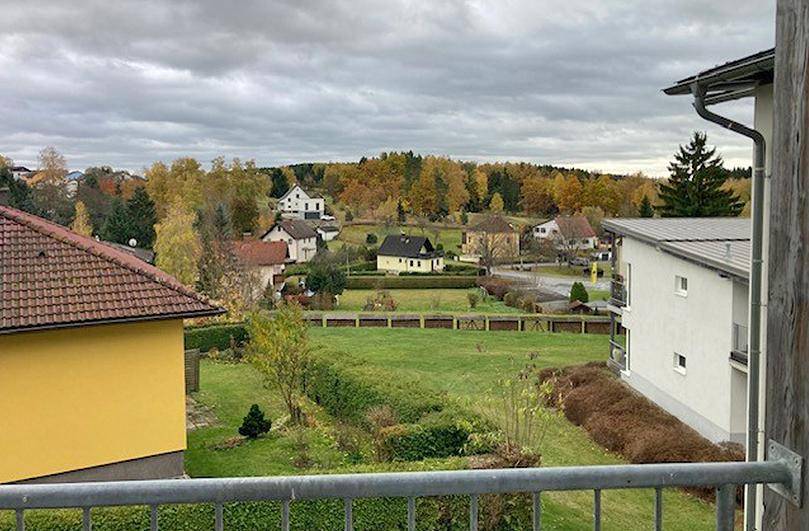 Weitläufiger Blick von einem Balkon auf eine ländliche Umgebung mit Häusern und Herbstbäumen.