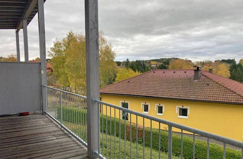 Balkon mit Holzboden und Metallgeländer, bietet einen Blick auf benachbarte Häuser und Bäume.