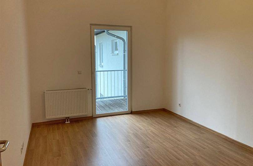 Schlichtes Zimmer mit Laminatboden, Heizkörper und Zugang zu einem französischen Balkon.