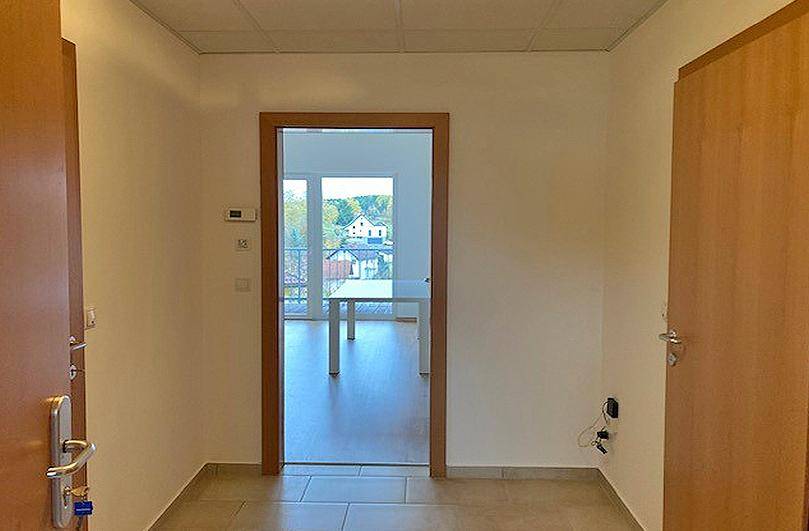 Heller Eingangsbereich mit Fliesenboden und Blick durch eine Holztür in einen weiteren Raum.