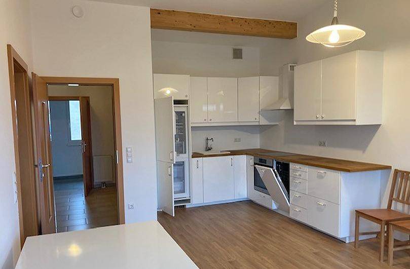 Moderne weiße Einbauküche mit Holztheke, integrierten Geräten und offenem Holzbalken.