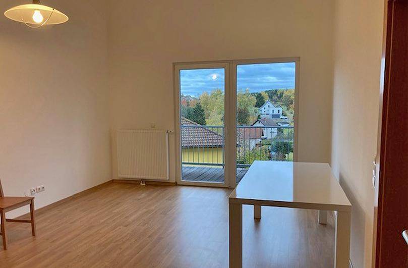 Heller Wohnbereich mit Laminatboden, großem Fenster und Blick auf die umliegende Landschaft.
