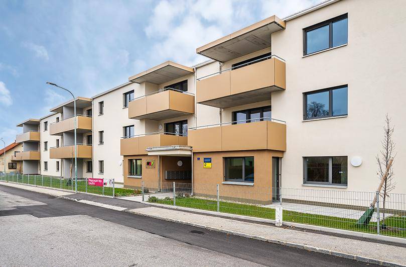 Moderne Fassade eines Mehrfamilienhauses mit Balkonen und gepflegtem Eingangsbereich unter blauem Himmel.