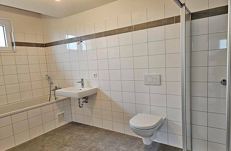 Helles Badezimmer mit Badewanne, Duschkabine, Waschbecken und Wand-WC.