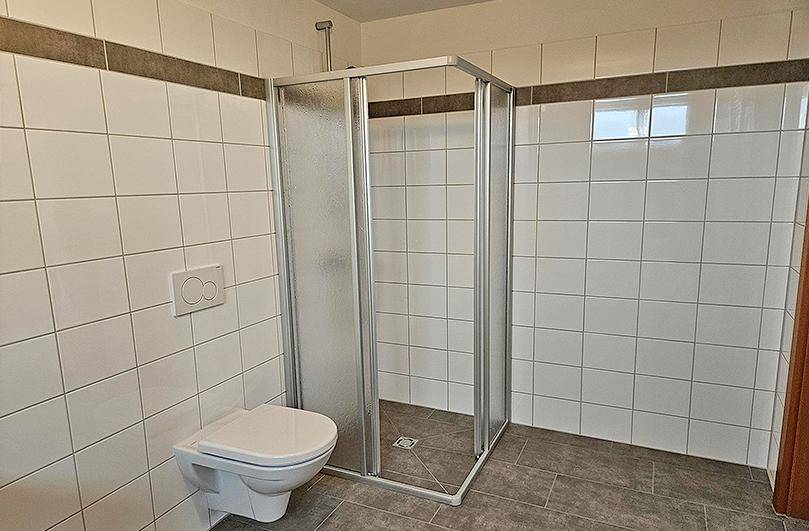 Modernes Badezimmer mit Duschkabine, Wand-WC und weißen Fliesen.