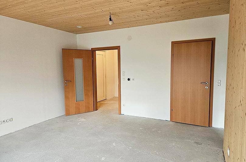 Heller Raum im Rohbau mit Holzdecke und mehreren Holztüren.