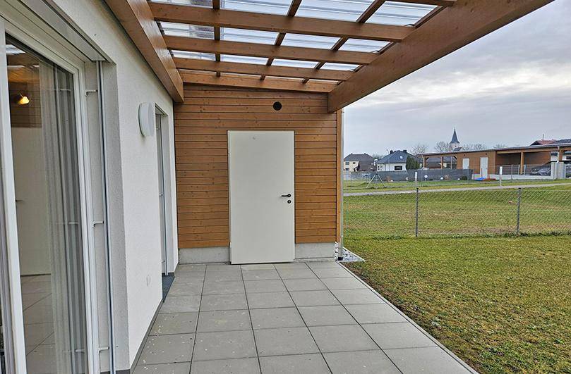 Überdachte Terrasse mit Zugang zu einem Abstellraum und Blick auf die Umgebung.