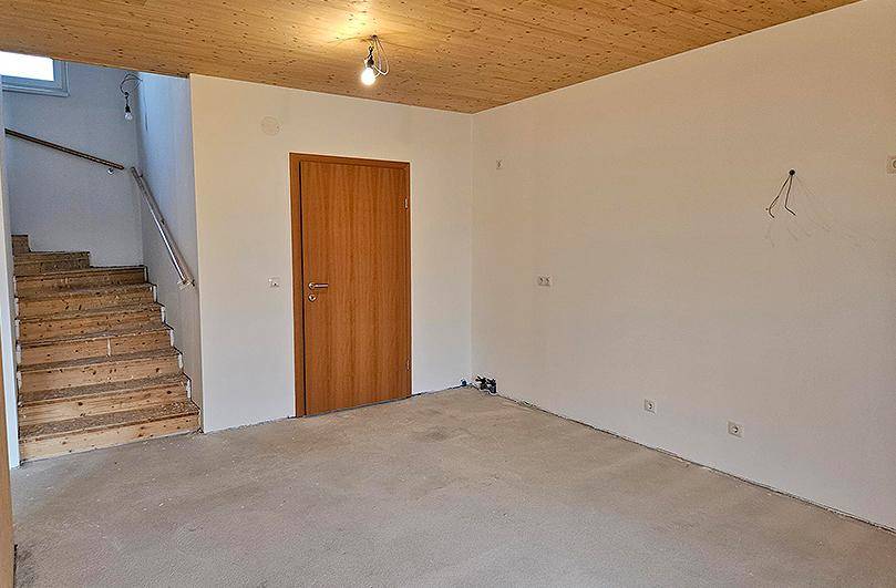 Geräumiger Raum im Rohbau mit Holzdecke und Treppenaufgang.