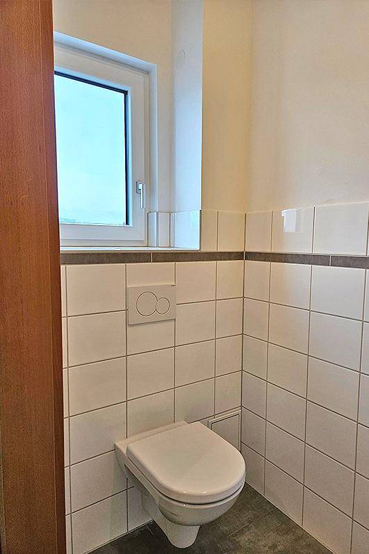 Kleines Gäste-WC mit Wand-WC, Fenster und weißen Fliesen.