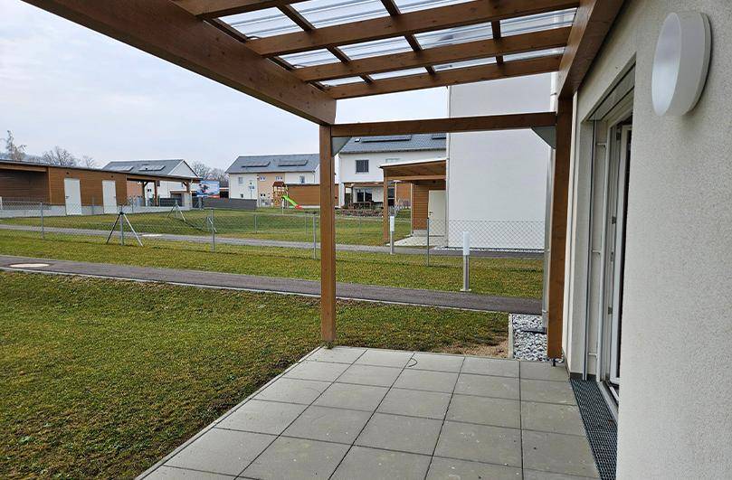 Überdachte Terrasse mit Pergola, Fliesenboden und Blick auf den Gartenbereich.