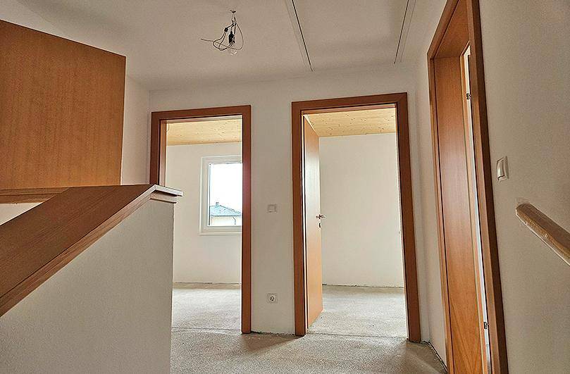 Flurbereich im Rohbau mit Holzdecke, Holztüren und Treppenaufgang.