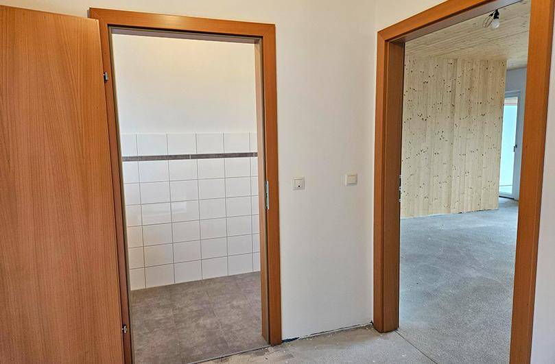 Flurbereich im Rohbau mit Holztüren und Blick in angrenzende Räume.