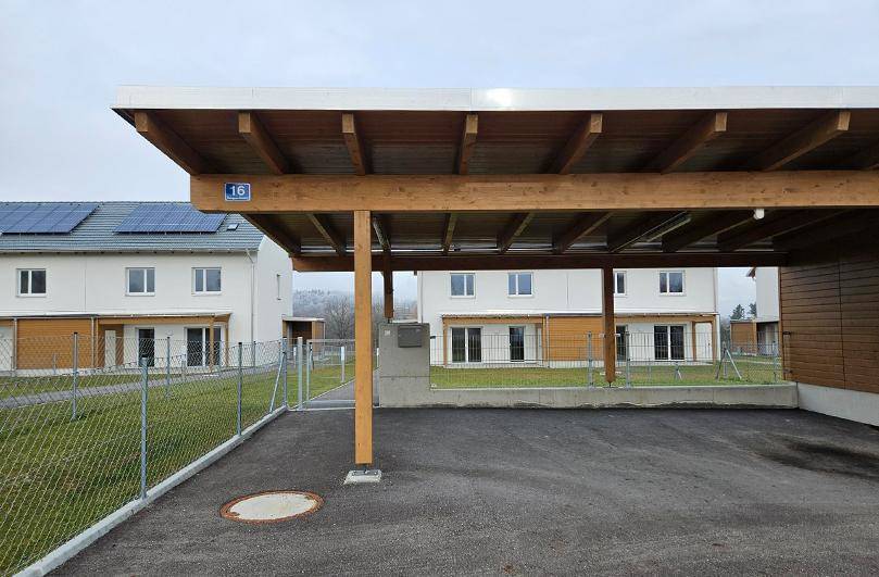 Moderner Carport aus Holz mit Blick auf die neu gebauten Doppelhäuser.