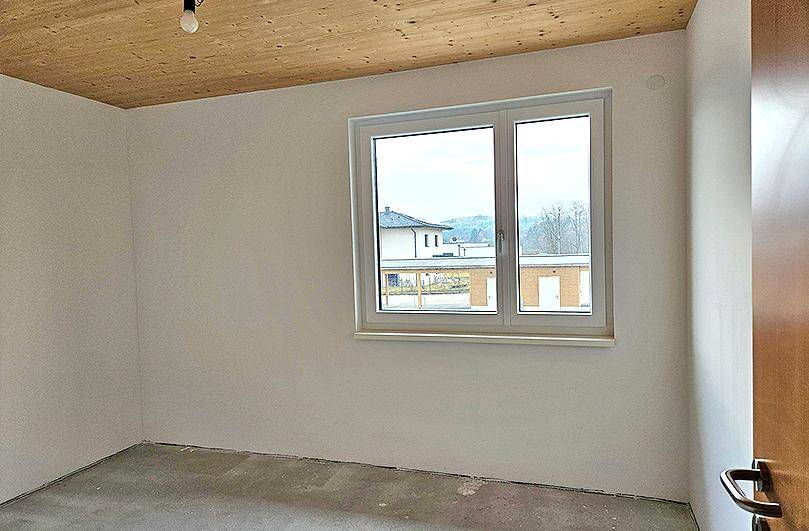 Schlafzimmer im Rohbau mit Holzdecke, Fenster und Blick auf die Nachbarschaft.