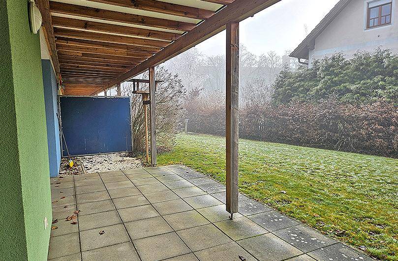 Überdachte Terrasse mit Fliesenboden und Zugang zu einem gepflegten Gartenbereich.