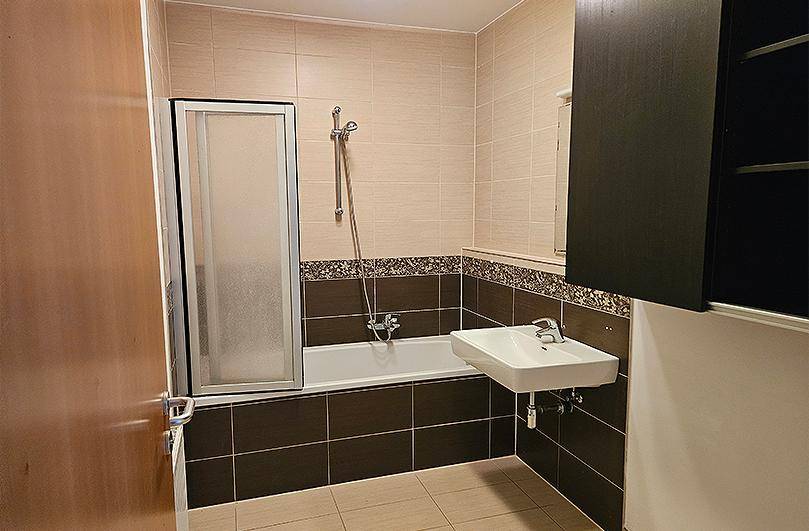 Badezimmer mit Badewanne, Duschvorrichtung, Waschbecken und beigefarbenen Fliesen.