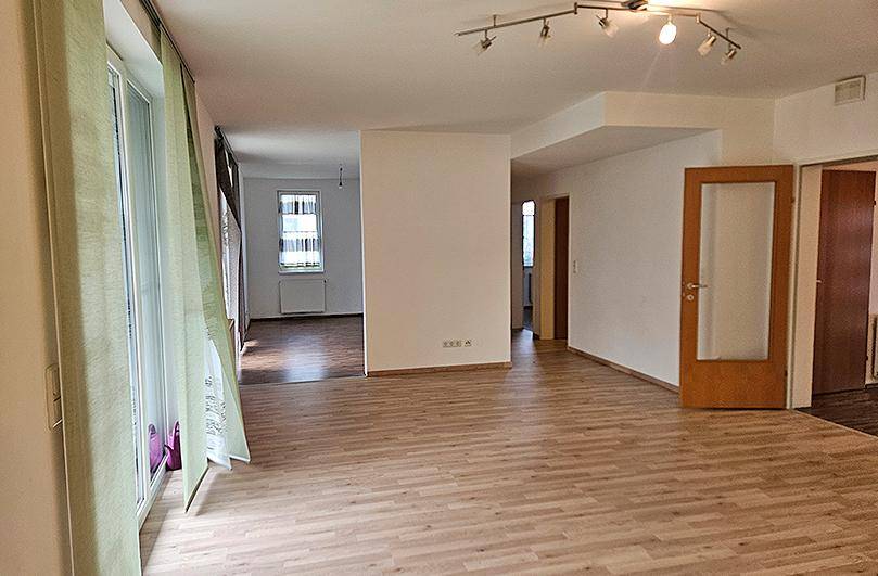 Heller Wohnbereich mit Laminatboden, weißen Wänden und Zugang zu weiteren Zimmern.