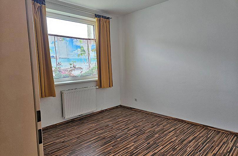 Schlafzimmer mit Laminatboden, weiß gestrichenen Wänden und einem Fenster mit Vorhängen.