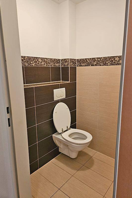 Separate Toilette mit Wand-WC und beigefarbenen sowie braunen Fliesen.