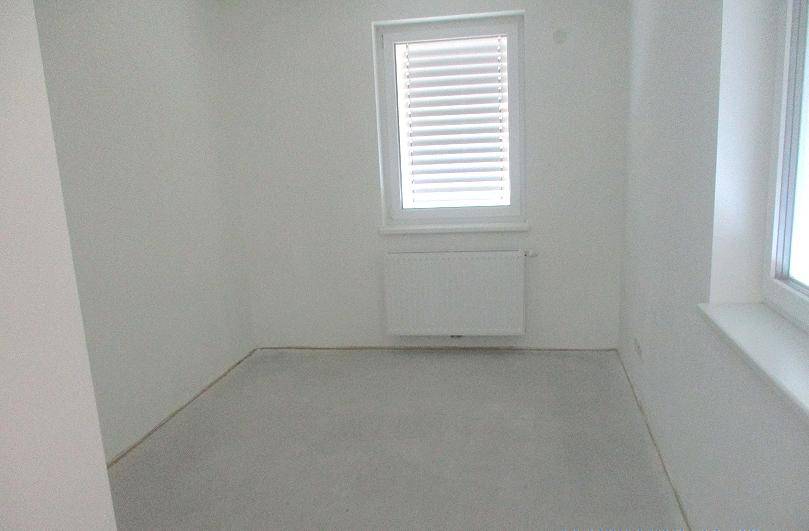 Leerer Raum mit weiß gestrichenen Wänden, einem Fenster mit Jalousien und einem Heizkörper.