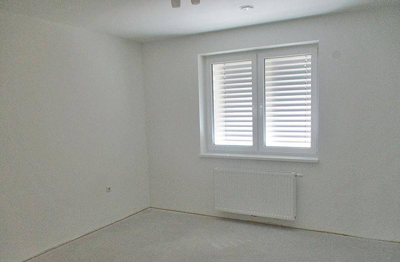 Leerer Raum mit weiß gestrichenen Wänden, einem Fenster mit Jalousien und einem Heizkörper.