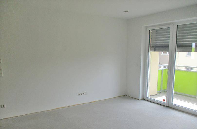 Heller, leerer Raum mit Zugang zu einem Balkon und weiß gestrichenen Wänden.