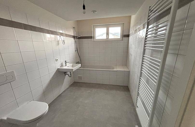 Helles Badezimmer mit weißen Fliesen, Badewanne, Dusche und beheiztem Handtuchhalter.