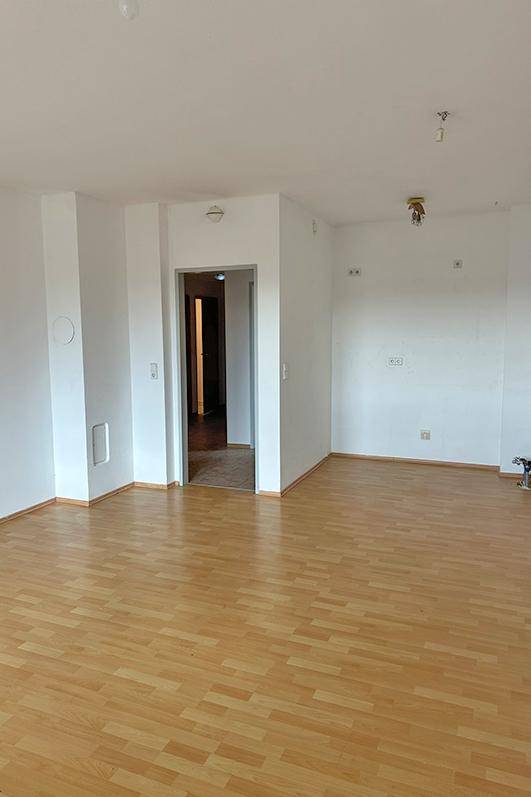 Geräumiges Wohnzimmer mit hellem Laminatboden und weißen Wänden.