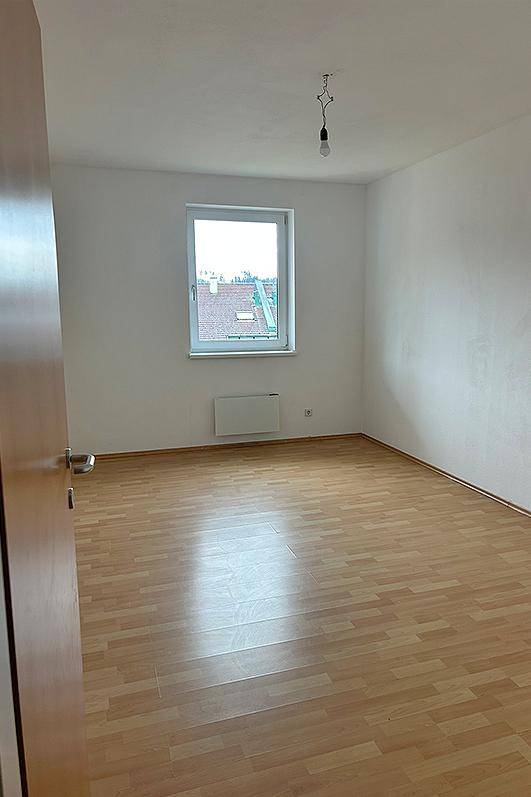 Leeres Schlafzimmer mit Laminatboden und einem Fenster mit Blick auf Dächer.