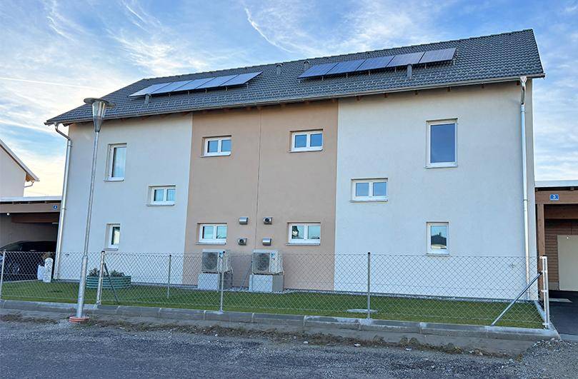 Neubau-Reihenhaus mit moderner Fassade, Photovoltaikanlage und Wärmepumpen im Außenbereich.