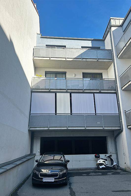 Rückansicht des Gebäudes mit mehreren Balkonen und einem geparkten Auto unter blauem Himmel.