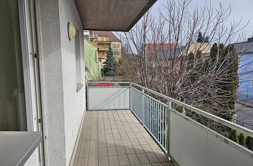 Heller Balkon mit Metallgeländer und Blick auf die Nachbarschaft und Bäume.
