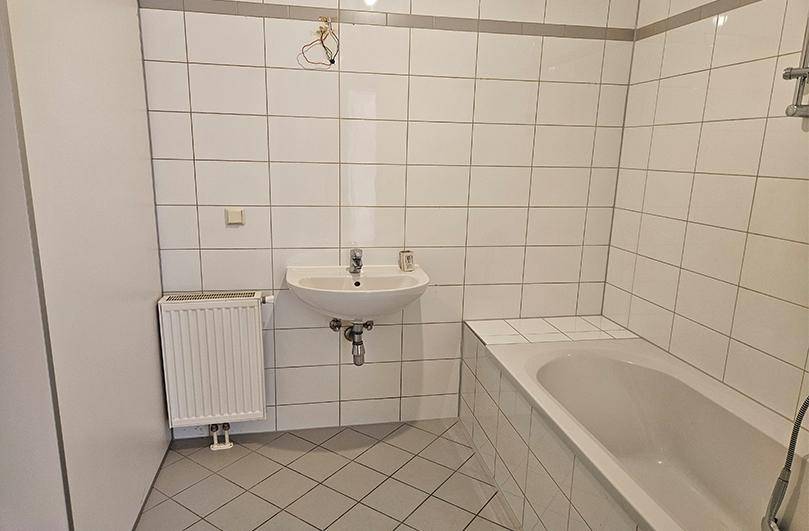 Badezimmer mit Badewanne, Waschbecken und weißen Fliesen, bereit für die Endmontage.