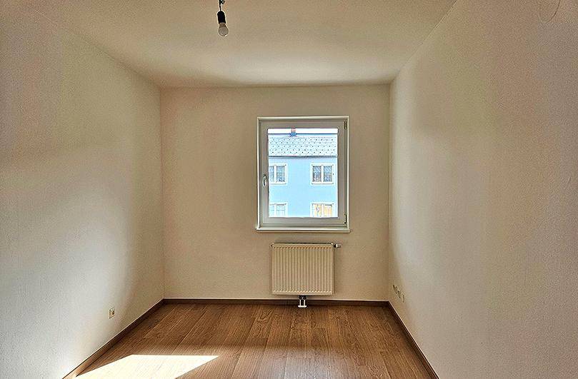 Ruhiges Zimmer mit Laminatboden und großem Fenster, das viel Tageslicht hereinlässt.