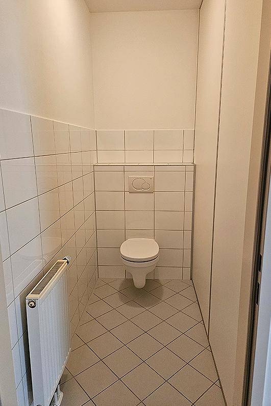 Separates WC mit Wandtoilette, Heizkörper und weißen Wandfliesen.