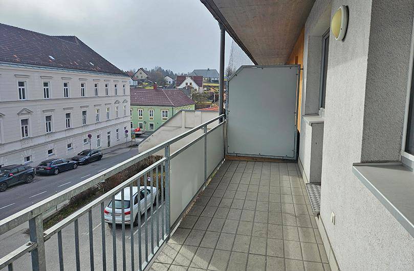 Geräumiger Balkon mit Fliesenboden und Blick auf die Straße und umliegende Gebäude.
