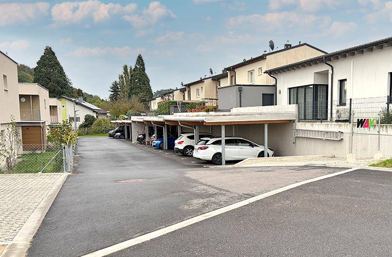 Reihenhäuser mit modernen Carports und asphaltierter Zufahrt in einer gepflegten Wohnsiedlung.