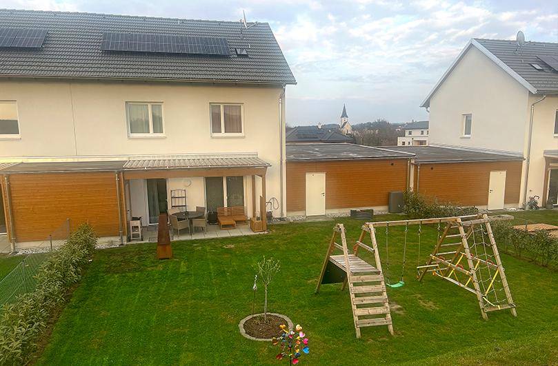 Großer Garten mit Rasenfläche, Spielplatz und überdachter Terrasse hinter dem Haus.