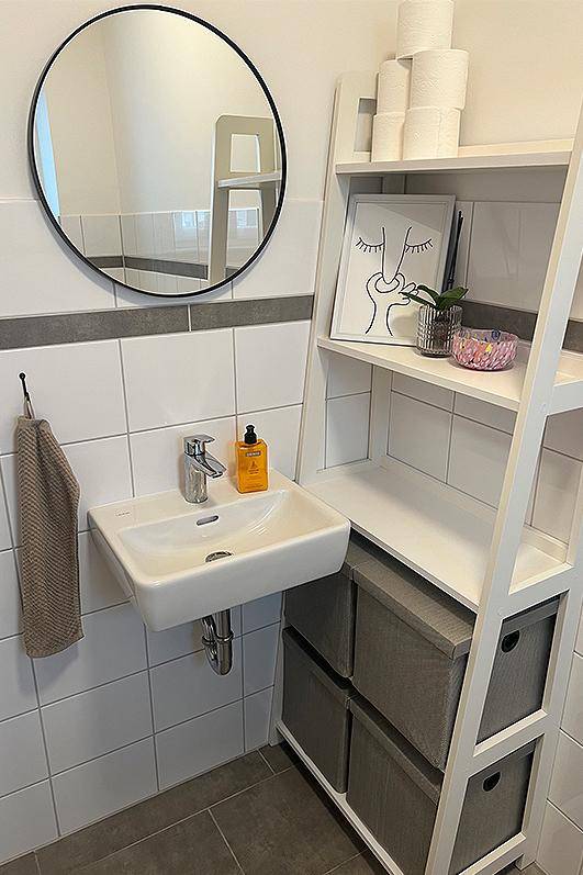 Modernes Gäste-WC mit kleinem Waschbecken, Spiegel und praktischem Regal.