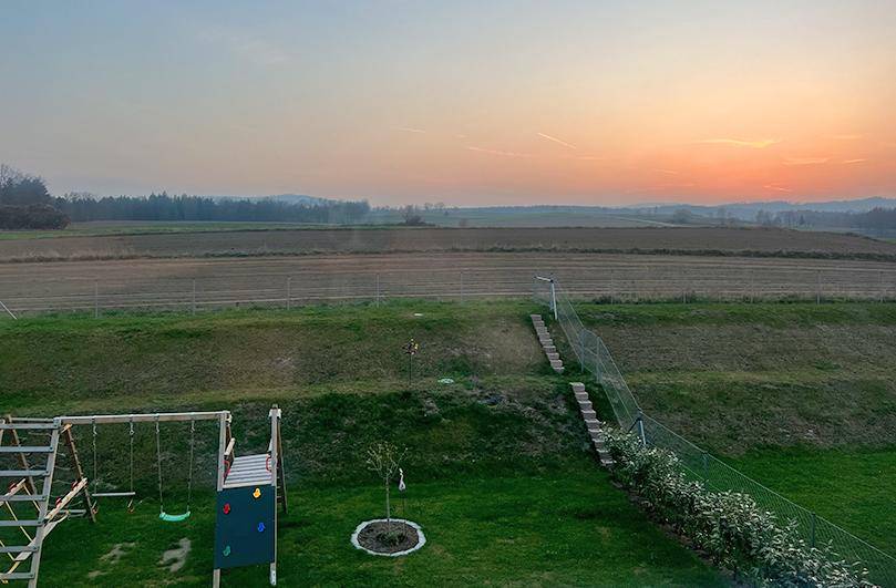 Weitläufiger Garten mit Spielplatz und freiem Blick auf die umliegende Landschaft bei Sonnenuntergang.