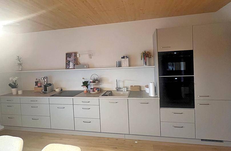 Moderne Einbauküche in hellem Grau mit integrierten Geräten und Holzdecke.