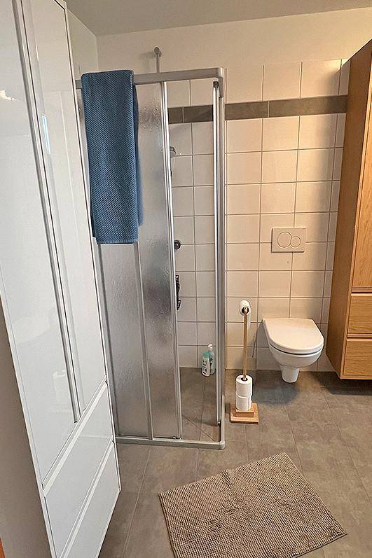 Badezimmer mit Duschkabine, wandhängendem WC und praktischem Holzschrank.