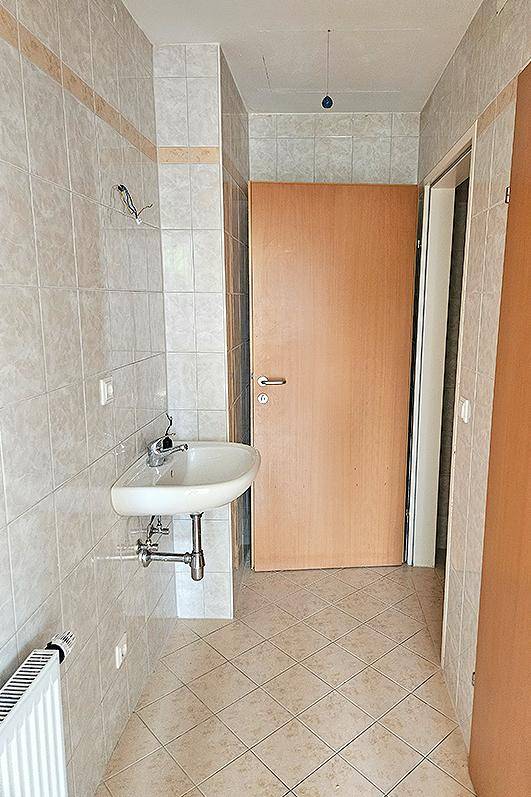 Heller Flur mit Fliesenboden, Waschbecken und Heizkörper, führt zu weiteren Räumen.