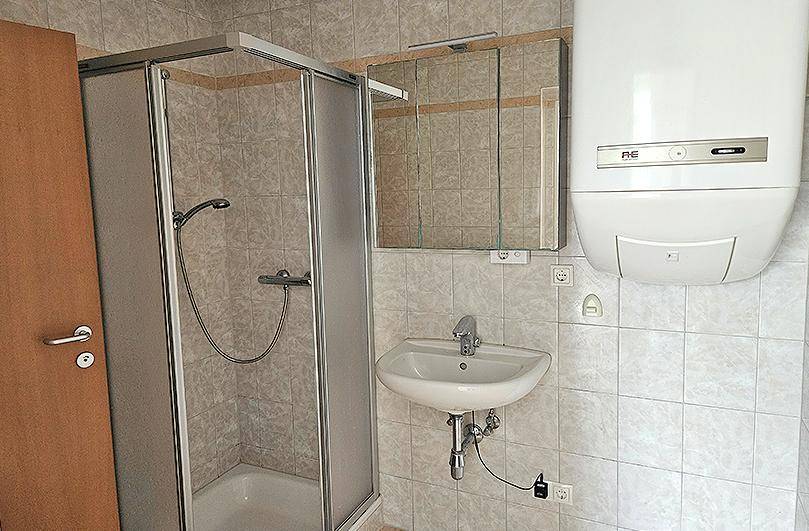Gefliestes Badezimmer mit Duschkabine, Waschbecken und Spiegelschrank, inklusive Warmwasserboiler.