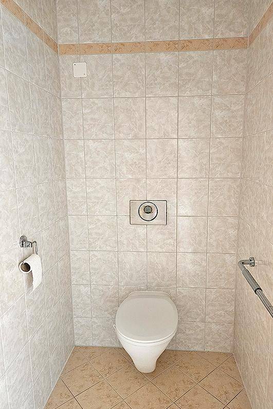 Separate Toilette mit Wand-WC und hellen Fliesen, ausgestattet mit Haltegriff für Komfort.